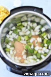 Frozen chicken, chopped onions, and celery in water inside an Instant Pot, perfect for starting Instant Pot Chicken Noodle Soup with Frozen Chicken.