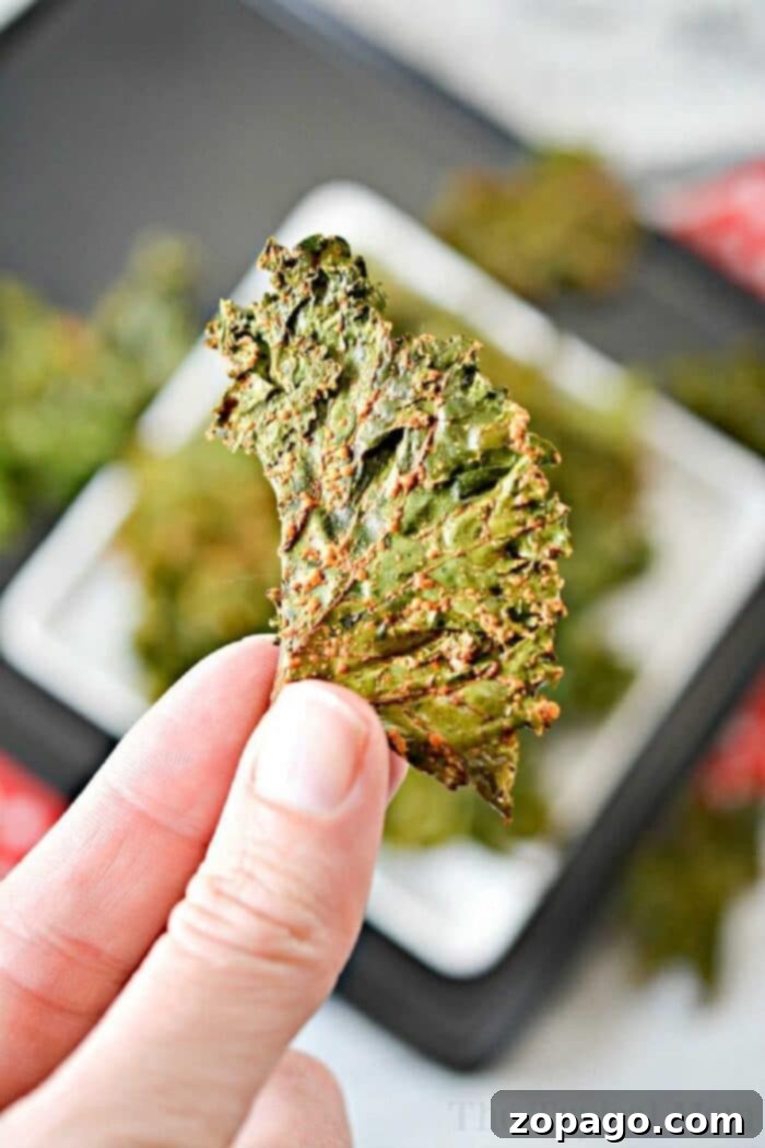 Easy kale chips recipe for those of you, like me, who weren't believers. They really are good and tasty, even my kids liked them! #kale #kalechips #ranchkalechips how-to-make-kale-chips in the oven, with a full bowl of green, crunchy kale chips on a wooden board, garnished with a sprinkle of herbs.
