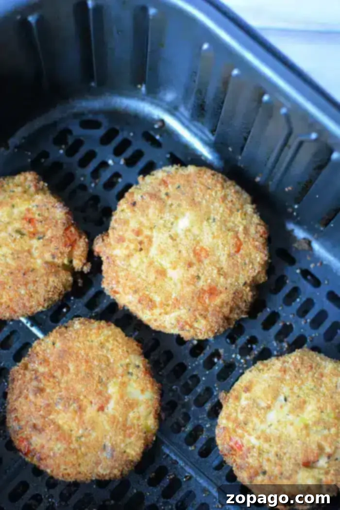 Golden Crispy Air Fryer Crab Cakes 8 Four perfectly breaded and golden-brown crab cakes are nestled within the dark, nonstick basket of an air fryer, ready for the final stages of cooking. The crisp exterior of each patty is clearly visible, promising a delightful crunch.