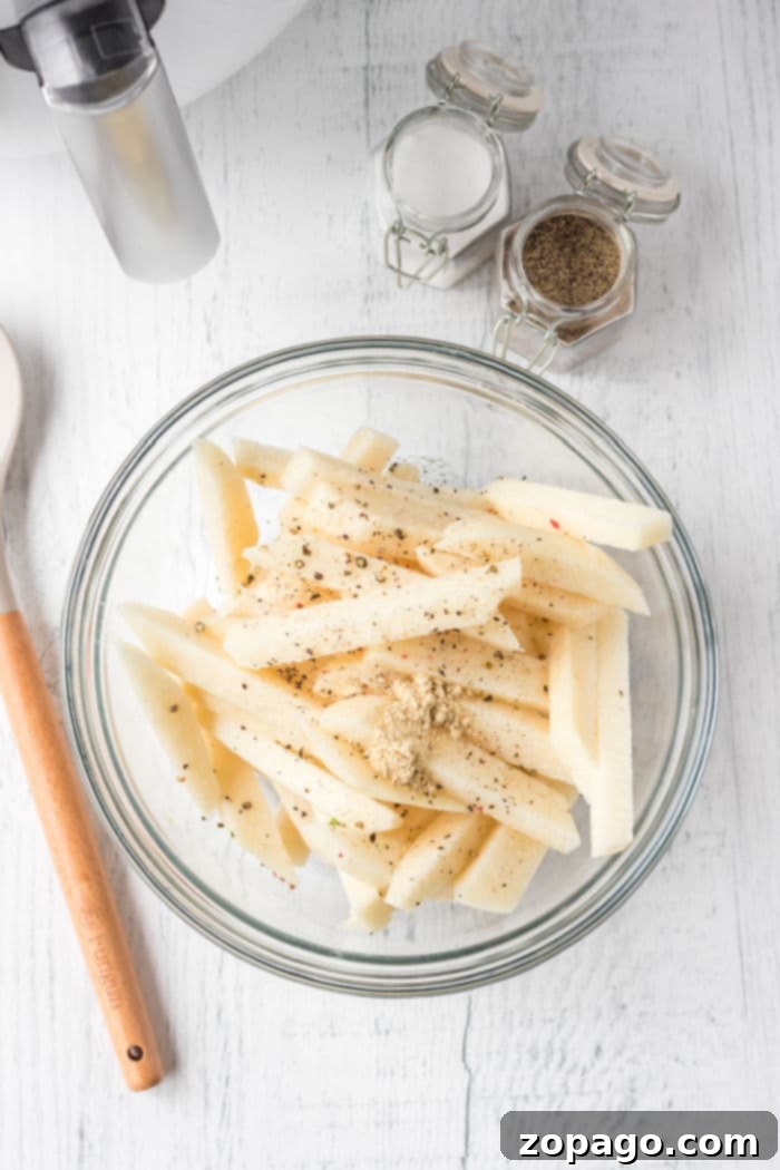 Crispy Jicama Fries 3 A glass bowl holds air fryer jicama fries, seasoned to perfection with spices and herbs, while a wooden spoon and spice jars rest nearby.