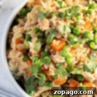 Savory Instant Pot Chicken Thighs and Rice 5 A bowl of fried rice with peas, carrots, and chopped herbs on top, set on a striped cloth, perfectly complements the savory flavors of instant pot chicken thighs.