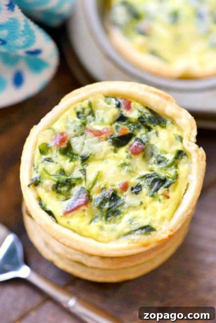An easy mini quiche recipe featuring a delightful spinach and bacon filling, elegantly presented on a wooden surface beside a small spoon.