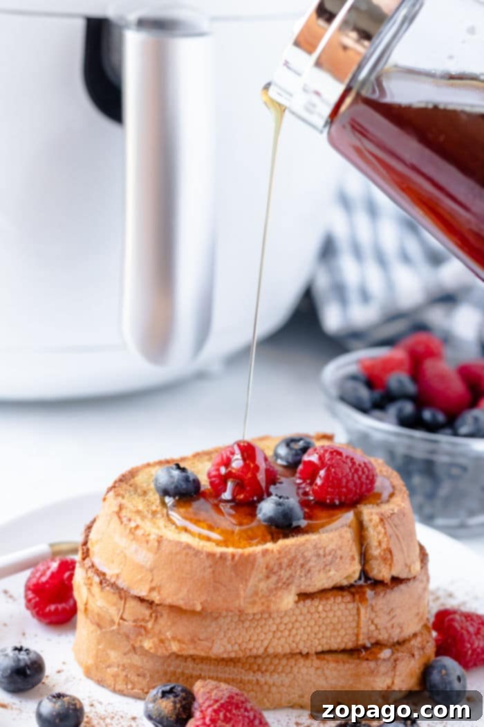 Easy Air Fryer French Toast 7 Stack of air fryer French toast, perfectly crisped, topped with fresh berries and drizzled with syrup, with extra berries in the background.