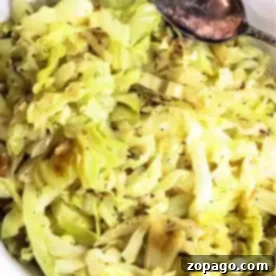 Easy Slow Cooker Cabbage 6 A white plate filled with slow cooker cabbage, seasoned with black pepper. A silver spoon rests on the edge of the plate.
