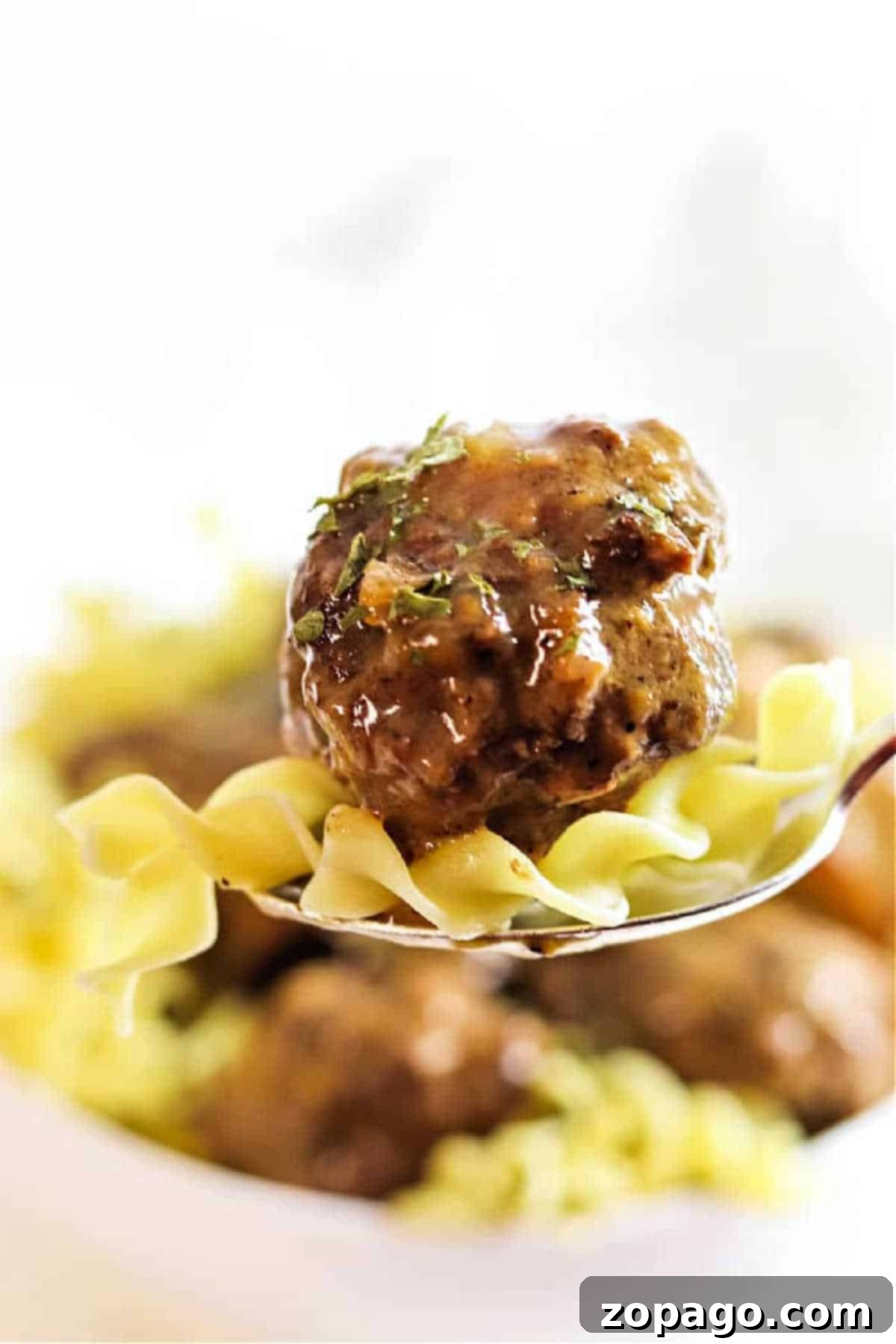 Slow Cooker Meatballs Smothered in Gravy 2 Close-up of a fork with a meatball and noodles, garnished with herbs, evokes the comforting flavors of Crockpot Meatballs and Gravy.