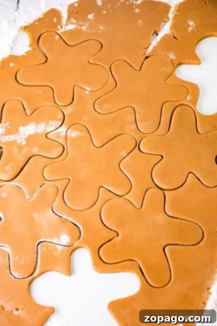 Perfectly Spiced Gingerbread Dough 5 Close-up of rolled-out gingerbread dough with flower-shaped cutouts. The dough is light brown with a few flour patches on the surface. Some cutouts are fully formed, while others remain connected to the surrounding dough.