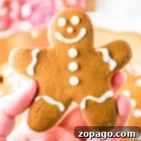 A hand holding a smiling gingerbread cookie crafted from rich gingerbread dough, adorned with delicate white icing decorations.