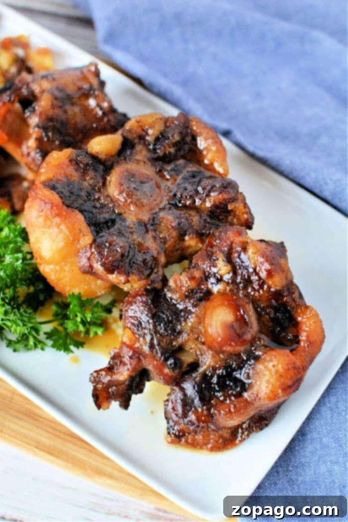 Fall-Off-The-Bone Oxtail 2 Close-up of oxtail pieces on a white plate, garnished with fresh parsley. This dish captures the rich flavors reminiscent of slow cooker oxtail perfection.