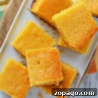 Top view of several pieces of Crockpot cornbread on a rectangular white plate, placed on a wooden cutting board.