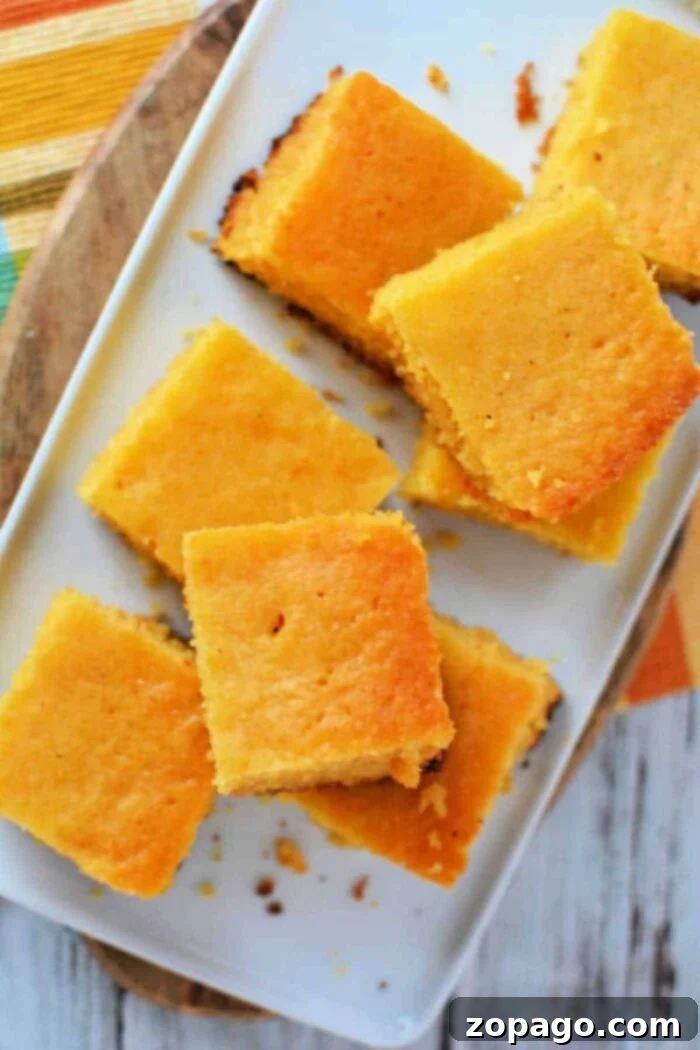 Effortless Slow Cooker Cornbread 9 Overhead view of a Crockpot cornbread recipe, golden brown and sliced into squares on a white serving plate.
