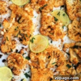 Roasted cauliflower steak slices, expertly spiced and air-fried to perfection, are garnished with lime and herbs on a pristine white surface.