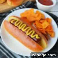 Frozen Hot Dogs Made Simple 7 Sizzling hot dog with mustard on a bun, served alongside crispy sweet potato chips and a side of ketchup on a checkered napkin. Perfectly complements your quest on how to cook frozen hot dogs to perfection.
