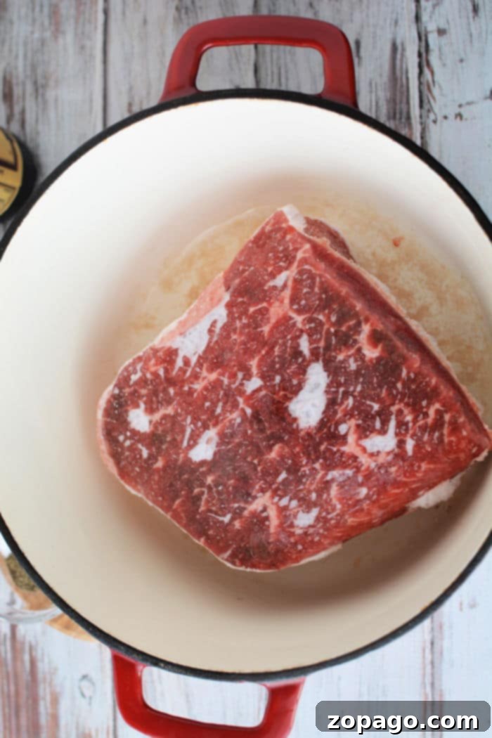 A Dutch oven containing a frozen roast with seasonings and liquid, ready for the oven.