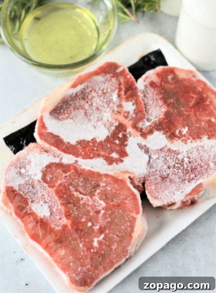 cooking Frozen Steaks - Three thick cut steaks, still frozen, sit ready for preparation on a white cutting board, alongside fresh rosemary and garlic.