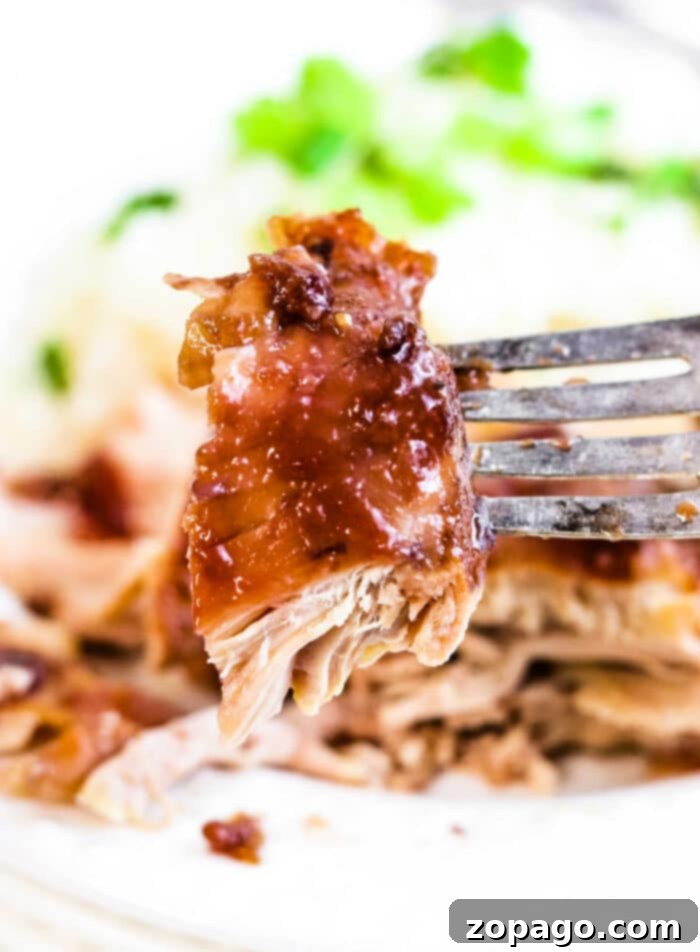 Melt-In-Your-Mouth Slow Cooker BBQ Chicken Thighs 8 A fork lifts a succulent piece of tender, shredded BBQ chicken, with a garnish of fresh herbs and blurred green background.