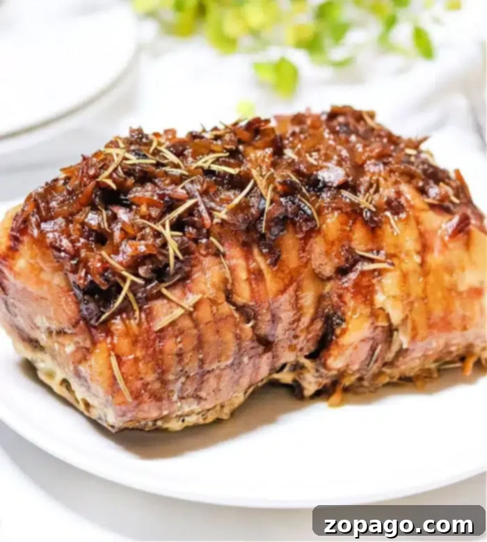 Savory Slow Cooker Pork with Onion 8 A cooked roast beef garnished with herbs and caramelized onions sits on a white plate, reminiscent of a hearty slow cooker pork roast. The meat appears juicy and is browned on the outside. In the background, there are hints of greenery and a blurred white object.