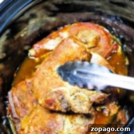 Slow Cooker Ranch Pork Chops 8 Close-up of Slow Cooker Ranch Pork Chops in a cooker, being lifted with metal tongs.