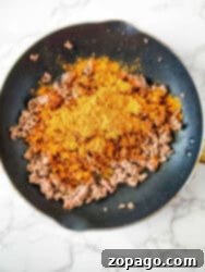 Effortless Slow Cooker Taco Meat 5 Seasoned ground meat in a frying pan, ready for the slow cooker.