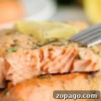 A close-up of grilled salmon with herbs, showcasing a fork revealing its flaky texture, alongside a lemon wedge. Perfectly executed even from frozen, this dish exemplifies how to cook frozen salmon to perfection.