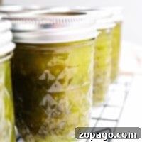 Close-up of sealed glass jars filled with a vibrant canned green pepper jelly, cooling on a metal rack.