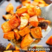 Close-up of roasted sweet potato cubes on a spatula, freshly pulled from the oven, with more pieces scattered on a baking sheet.