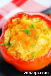 A delicious chicken stuffed red bell pepper with melted cheese and parsley sits elegantly on a black surface, complemented by a charming red-checkered cloth.
