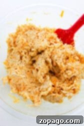 A glass bowl with shredded buffalo chicken dip being mixed by a red spatula, perfect for topping your chicken stuffed bell peppers.