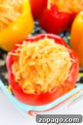 Chicken stuffed red and yellow bell peppers filled with cheese and rice, all nestled in a glass dish.