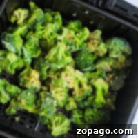 Frozen broccoli, perfectly seasoned, waits in the tray of an air fryer, ready to be cooked to crispy perfection.
