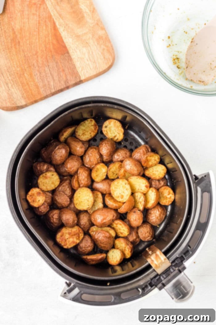 An air fryer basket filled with perfectly seasoned, crispy air fryer fried potatoes on a clean white surface.