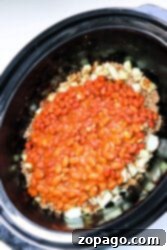 Close-up of a crockpot with venison chili, featuring baked beans, onions, and ground beef.