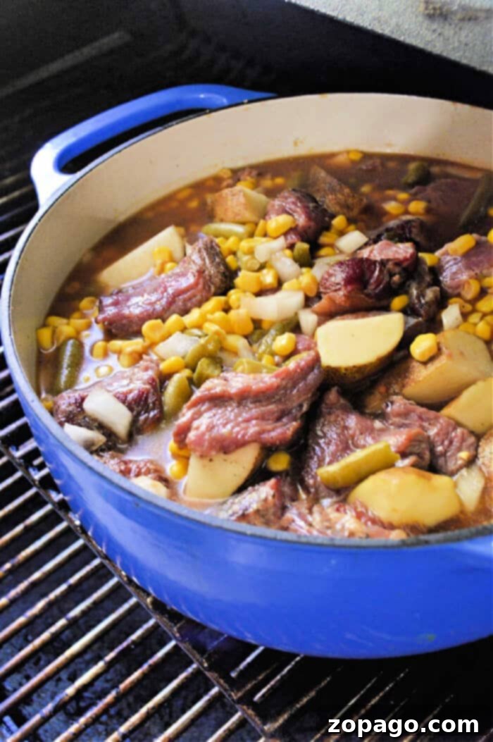 Slow-Smoked Stew 2 Blue pot with a smoky stew of beef stew meat, potatoes, corn, and diced vegetables simmering on the grill.