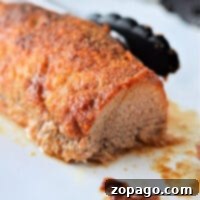 Sliced, seasoned pork tenderloin resting on a white surface with kitchen tongs in the background, showcasing the perfect result of learning how to cook Smithfield pork tenderloin.