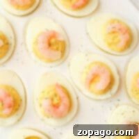 Shrimp deviled eggs are elegantly topped with succulent shrimp and sprinkled with fresh dill, all beautifully arranged on a pristine white plate.