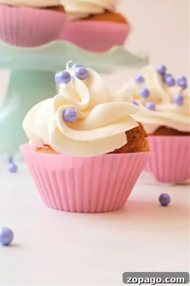 Easy Air Fryer Cupcakes 8 A close-up shot of an air fryer cupcake, beautifully adorned with a swirl of white frosting and shimmering purple pearl-like sprinkles, sitting in a vibrant pink silicone wrapper.
