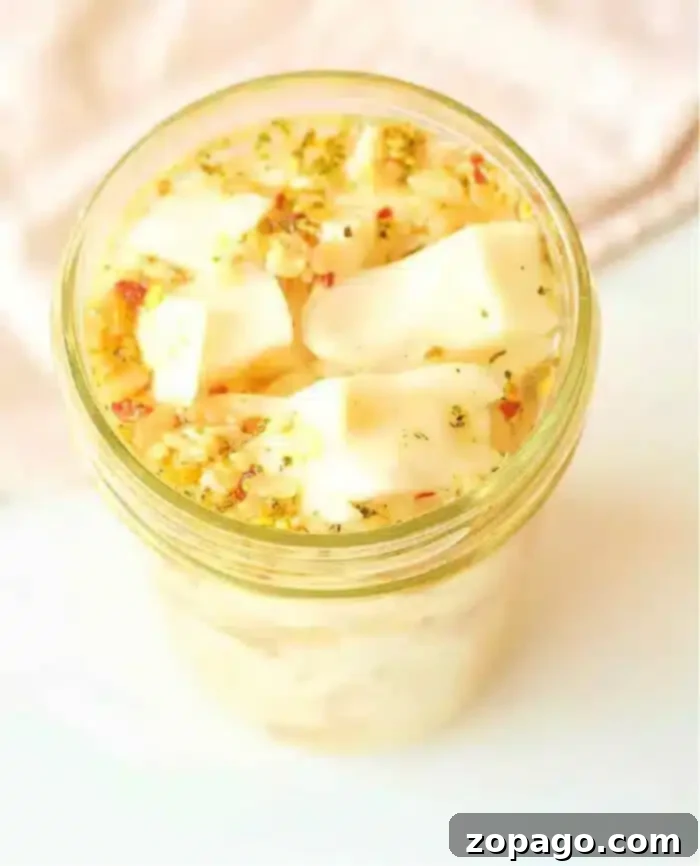 Speedy Tangy Cabbage 2 A jar filled with vibrant quick-pickled cabbage cubes, topped with fresh herbs and seasoning, sits alongside a batch of freshly prepared sliced cabbage, all captured from a high angle on a light-colored surface, inviting culinary exploration.
