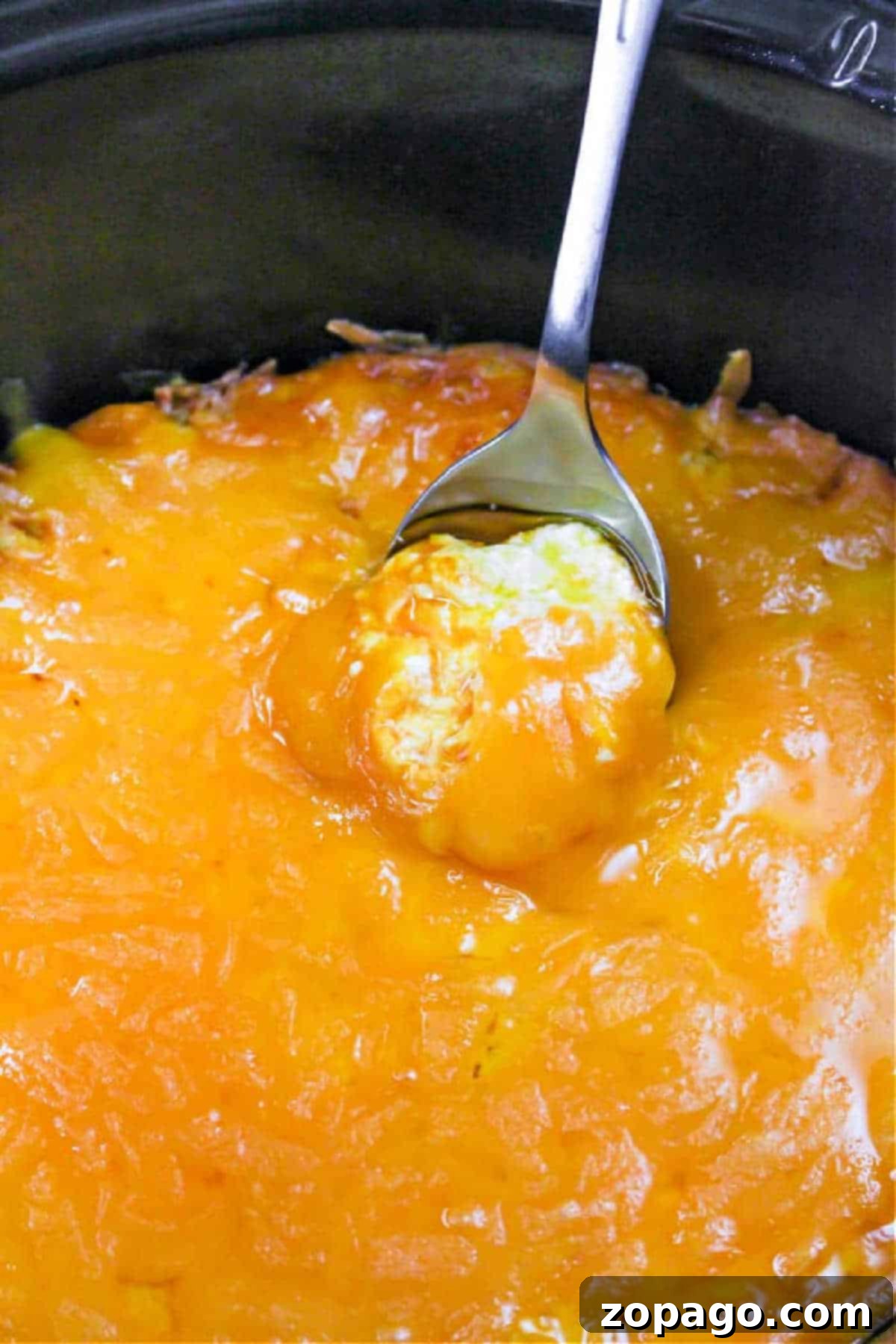 Publix-Style Buffalo Chicken Dip 2 A close-up of cheesy, golden-brown Buffalo Chicken Dip being scooped from a baking dish, highlighting its rich texture and appetizing appeal.