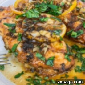 Effortless Italian Chicken Dinner 7 Chicken topped with lemon slices and chopped herbs rests elegantly on a white plate, embodying the zest of Crockpot Chicken enhanced with Italian Dressing.