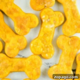 Air fryer dog treats, shaped like bones and delightfully orange, are neatly arranged on a white surface.