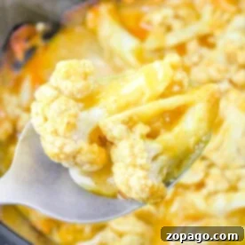 Close-up of a spoon holding Slow Cooker Cheesy Cauliflower, with tender florets smothered in a creamy yellow sauce.