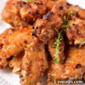 A plate of crispy, golden-brown chicken wings, perfectly suited for reheating in an air fryer, is garnished with fresh herbs.