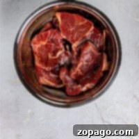 Raw beef pieces, perfectly sized for marination, resting in a metal bowl on a light gray surface, awaiting their Asian steak marinade.