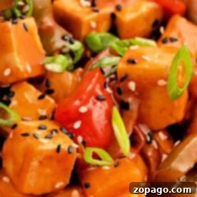 Close-up of sweet and sour tofu with bell peppers, sesame seeds, and sliced green onions, coated in a Copycat Panda Express Sweet and Sour Sauce.
