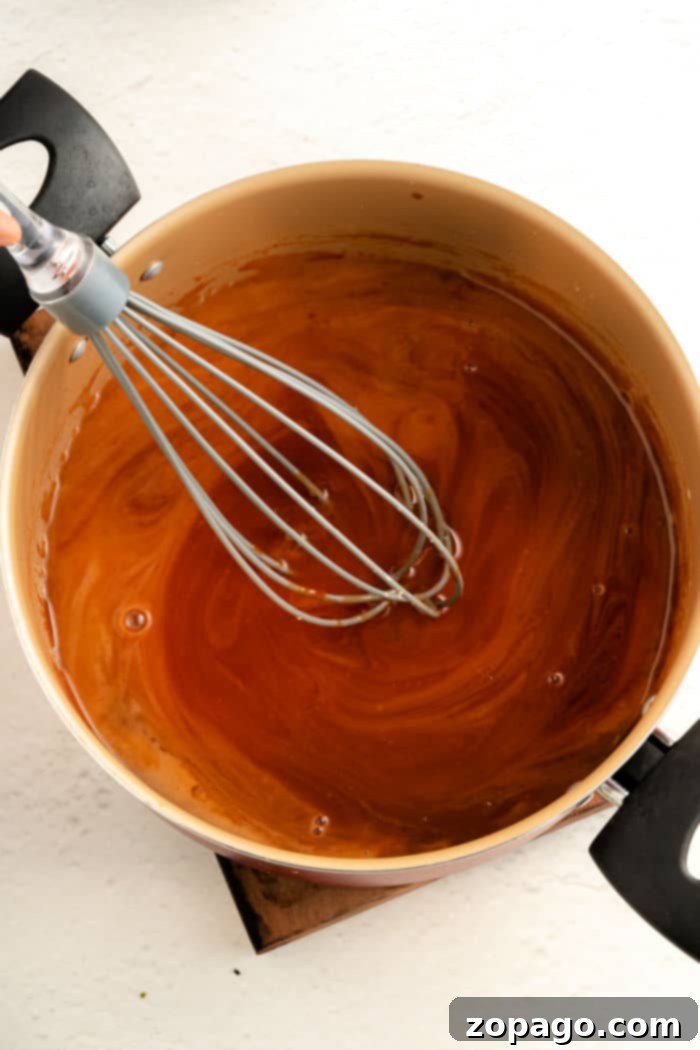 Authentic Panda Express Sweet and Sour Sauce From Your Kitchen 7 A pot of Panda Express Sweet and Sour Sauce, is being skillfully stirred with a whisk on the stove.
