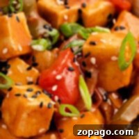 Close-up of spicy tofu stir-fry with green onions, bell peppers, and a sprinkle of sesame seeds, all brought together with a drizzle of copycat Panda Express sweet and sour sauce.