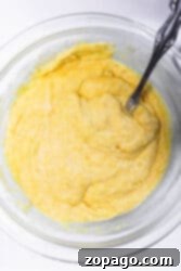 A glass bowl with yellow cornbread batter awaits a metal spoon, ready to transform this simple mixture into delightful corn dog bites.