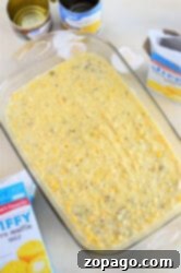 Glass dish with Jiffy Mexican Cornbread. Nearby are cans and a box of corn muffin mix on the countertop.