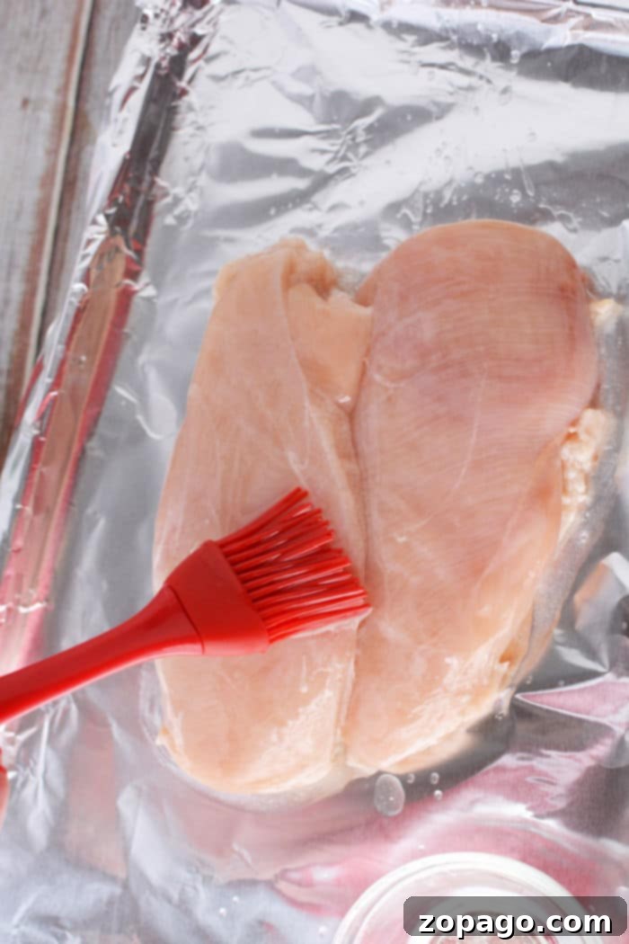 Effortless Oven-Baked Frozen Chicken Breast 4 Baking sheet with foil and olive oil drizzled chicken breasts, covered for baking