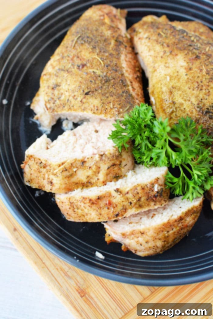 Effortless Oven-Baked Frozen Chicken Breast 6 Beautifully sliced roasted chicken breast, garnished with fresh parsley, on a dark plate, showing its tender and juicy interior after being cooked from frozen in the oven.