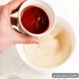 A hand hovers over a countertop, elegantly balancing a small bowl of thick red sauce above a creamy white sauce. It's the perfect palette for crafting your next culinary masterpiece: how to make Sriracha mayo.